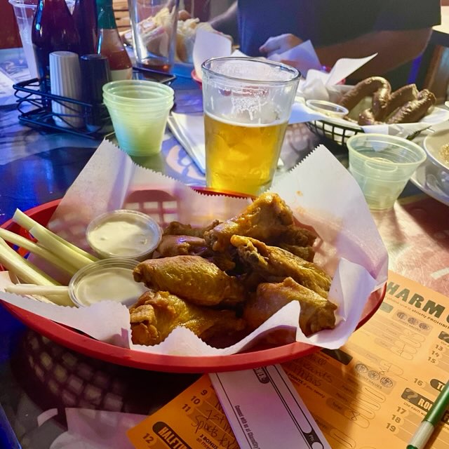 A basket of wings with celery and dipping sauce, a glass of beer, and a Charm City Trivia sheet and booklet