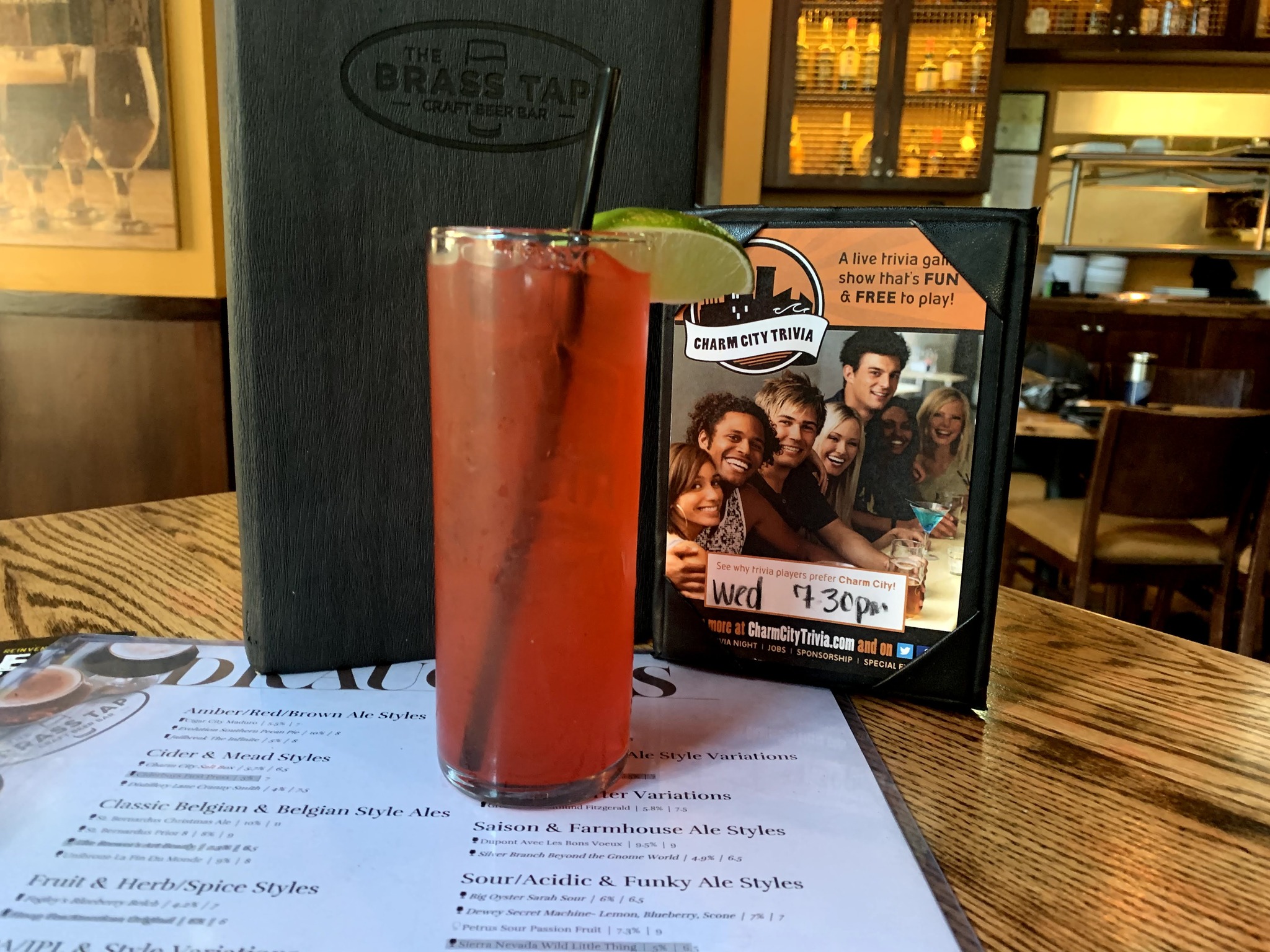 A red drink with a lime wedge sitting on a menu with a smaller menu displaying a Charm City Trivia advertisement