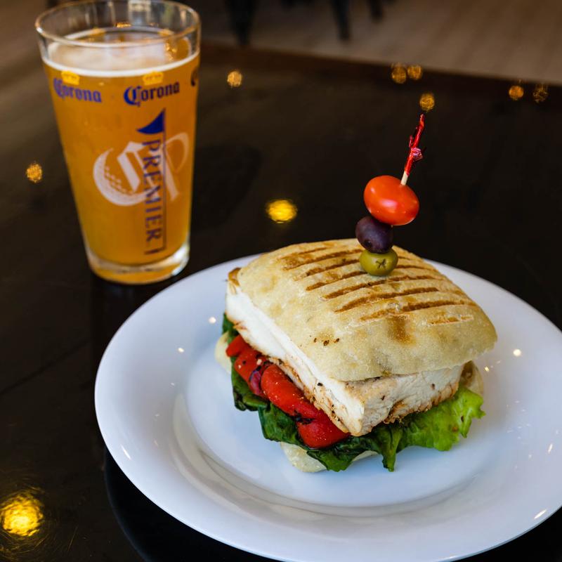 A chicken pesto panini sandwich with a glass of beer