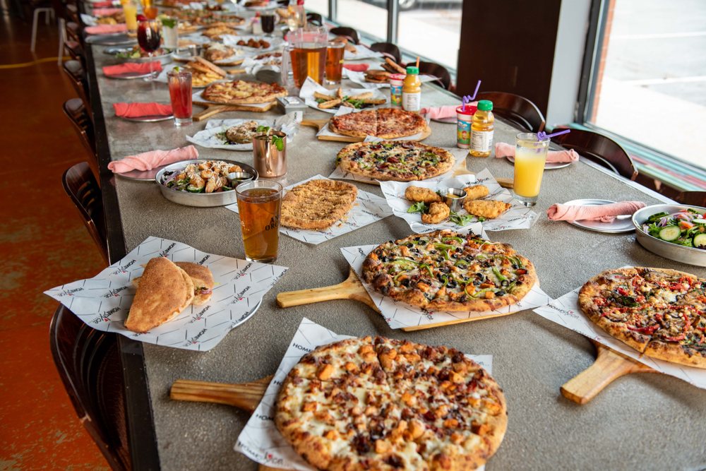 A long table with many pizzas, drinks, and other food