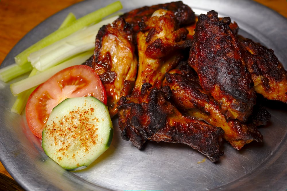 A plate of wings with celery, a tomato slice, and a cucumber slice