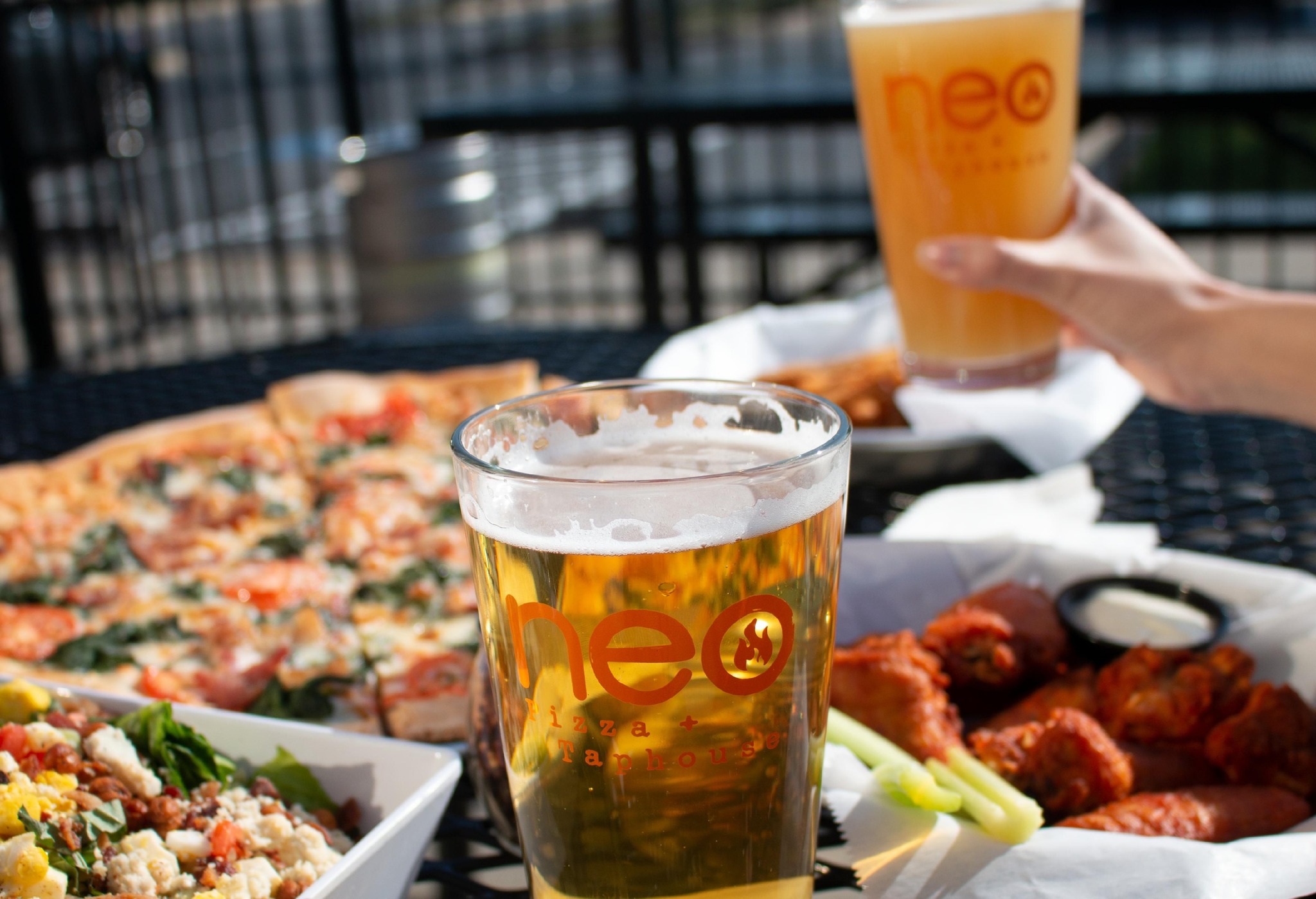 Several plates of food, including wings and pizza, with two glasses of beer