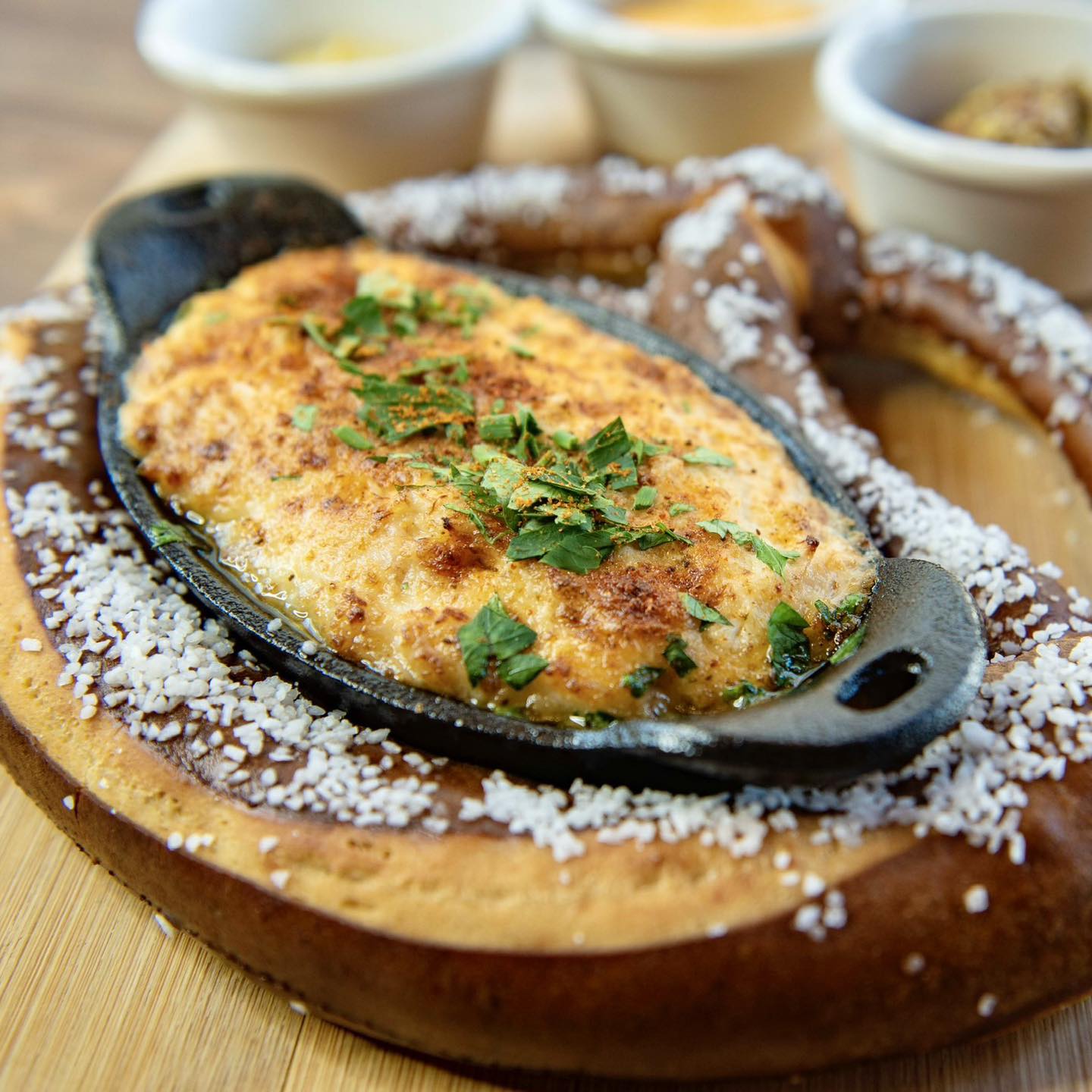 A soft pretzel with a bowl of crab dip