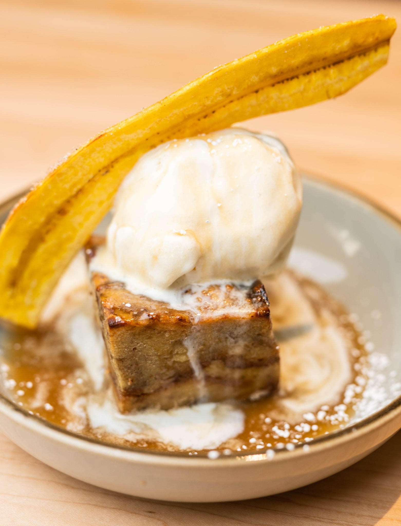 A plate of bananas foster bread pudding with a scoop of ice cream and half a banana cut long ways