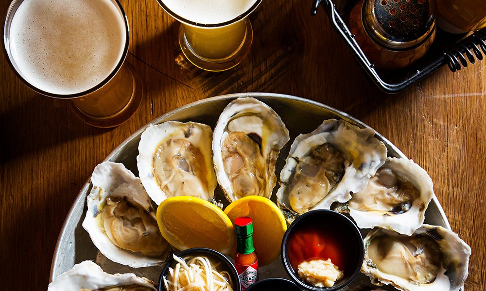 A plate of oysters with lemon halves and tabasco, and two glasses of beer