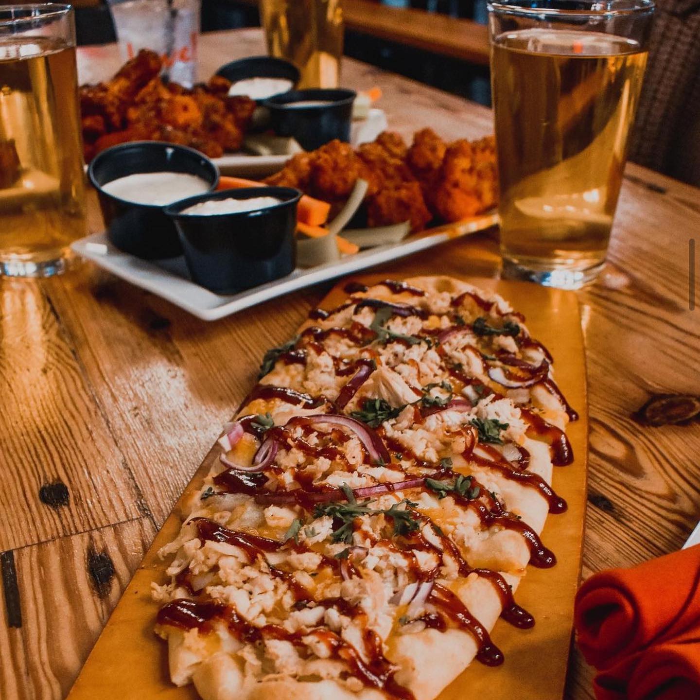 a barbecue chicken flatbread, a plate of wings, and two glasses of beer