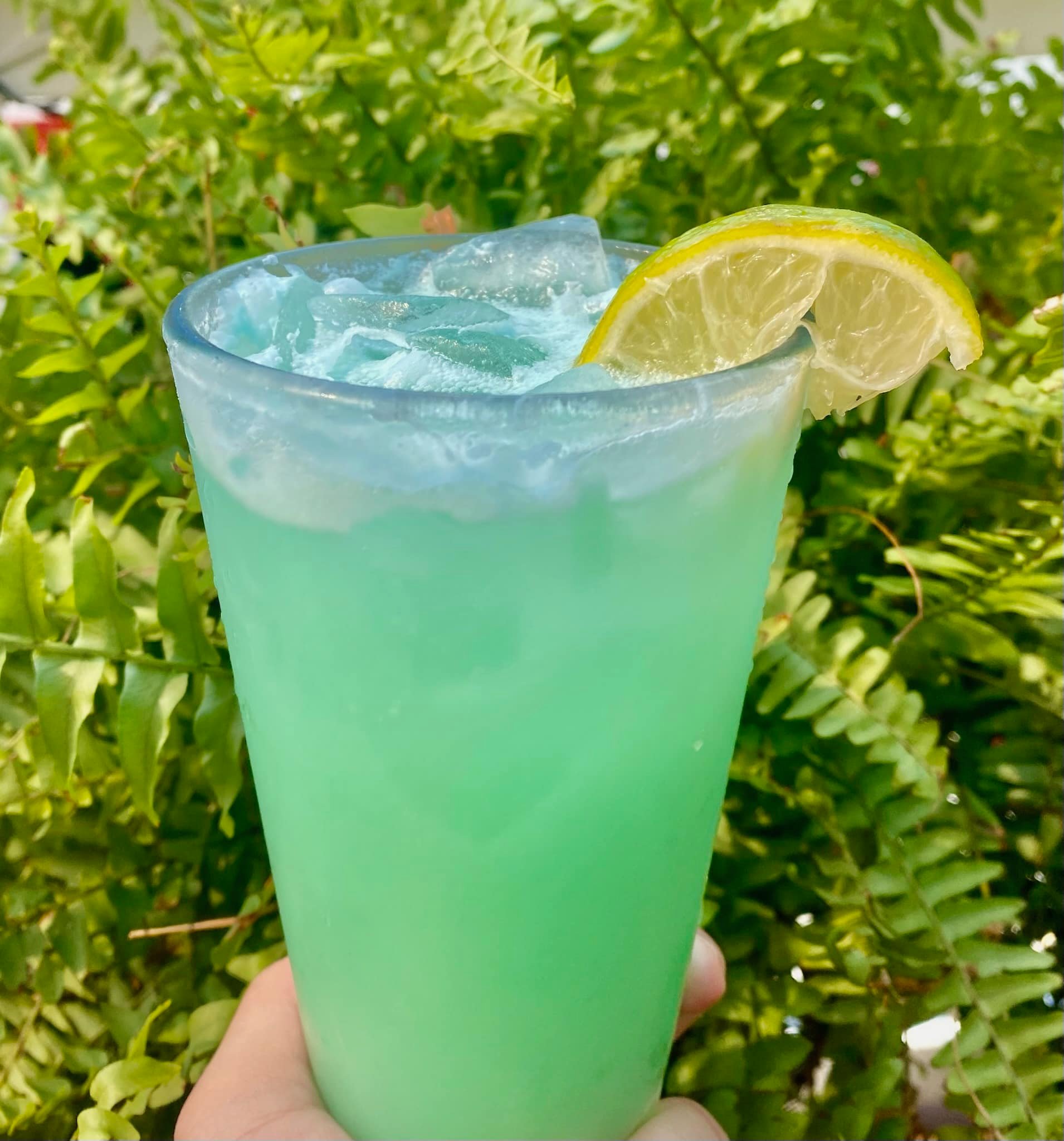 A glass of Loona-sea Crush, a teal cocktail with a lime wedge