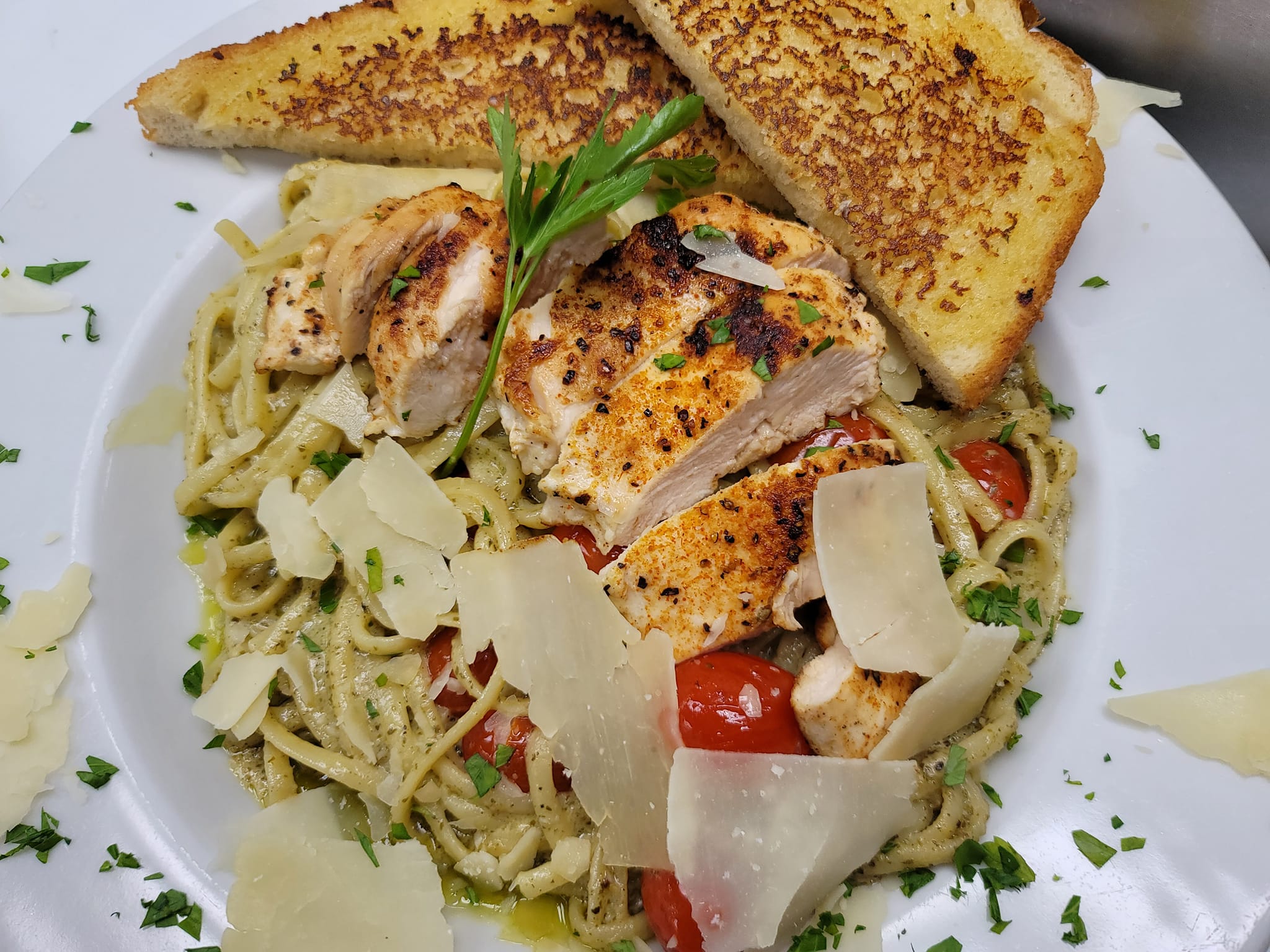 a bowl of pesto pasta with tomatoes, grilled chicken, parmesan, and toast