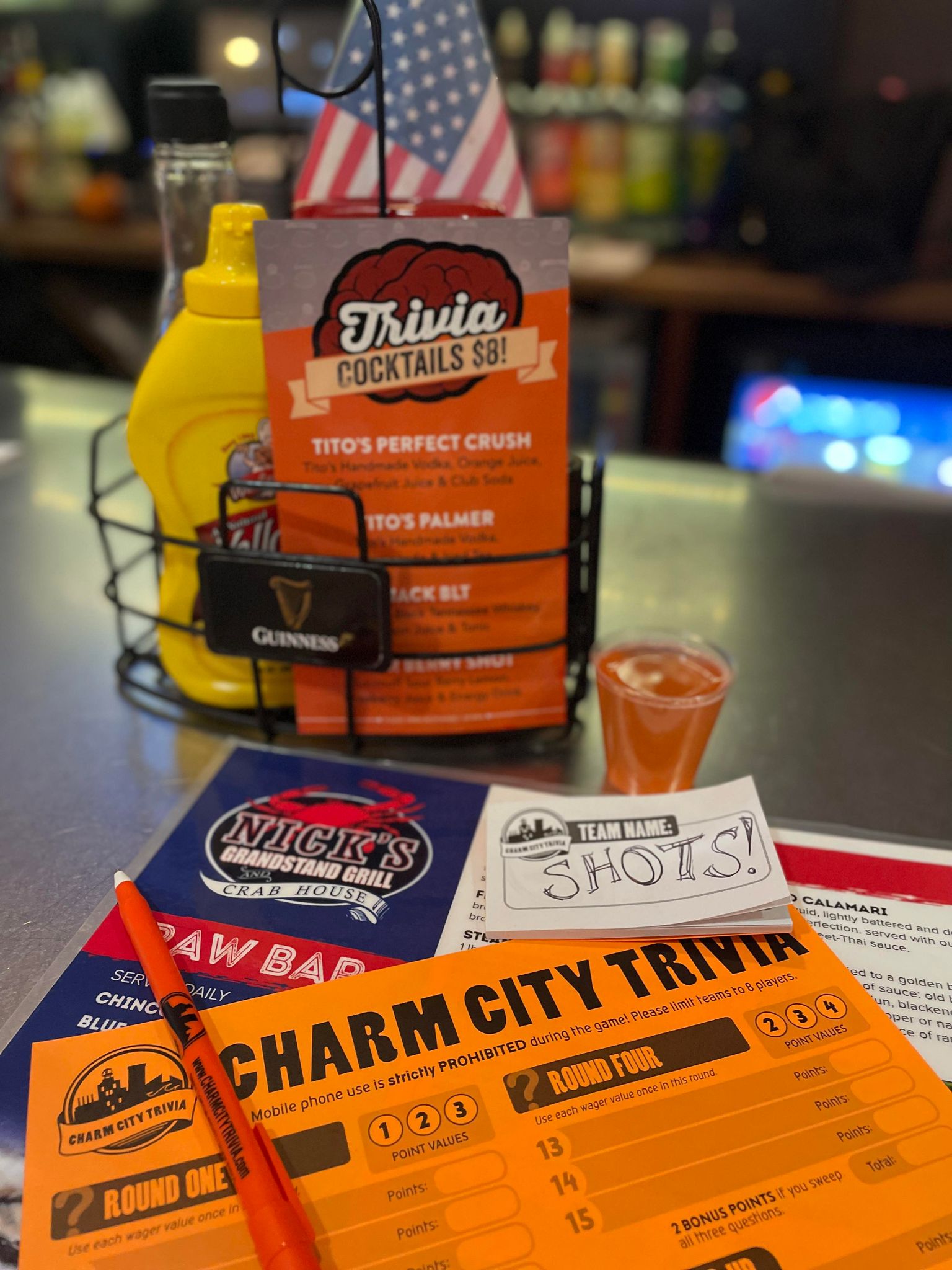 a charm city trivia player sheet and answer booklet on top of a menu, with a smaller menu that lists trivia cocktails