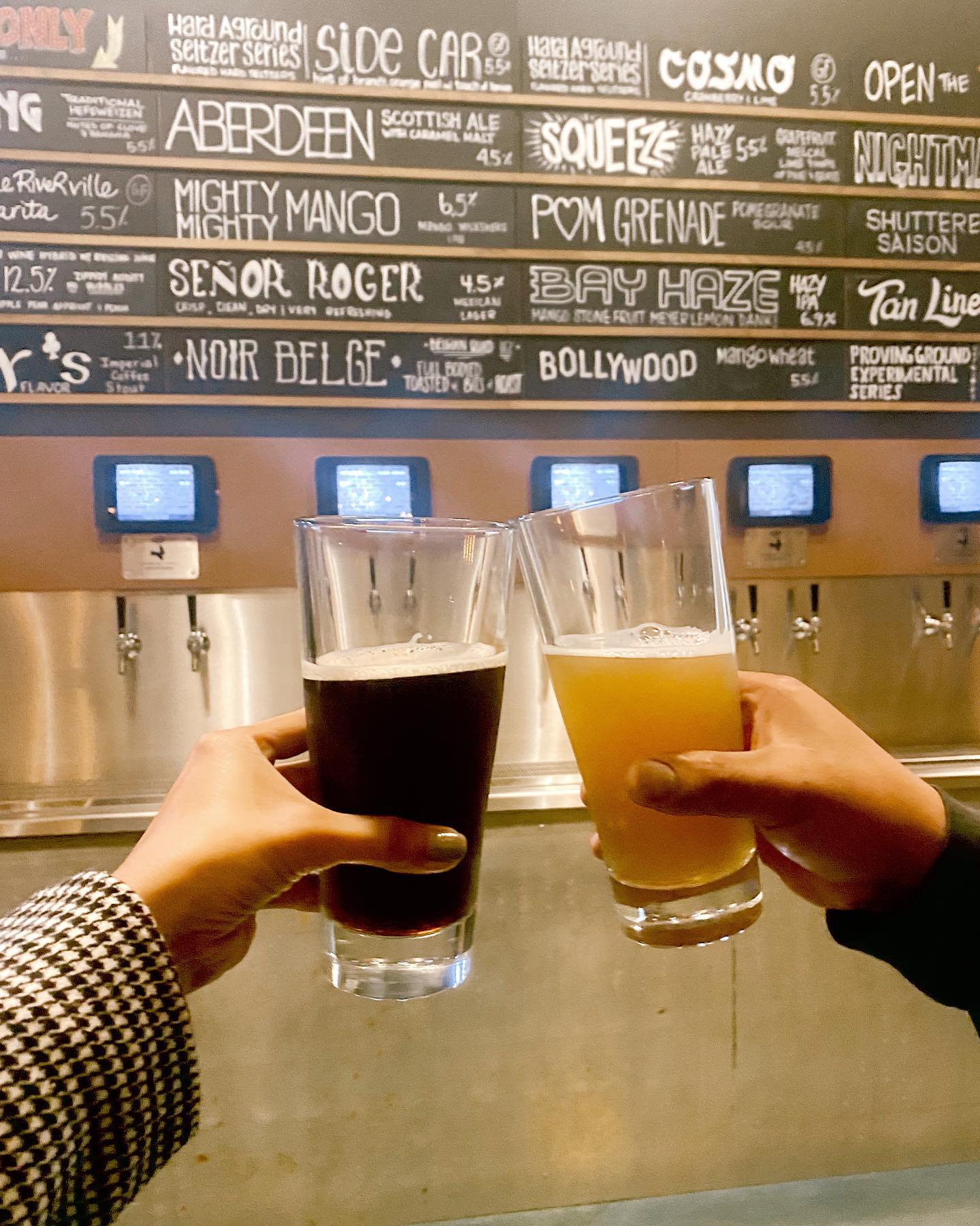 Two Beers being toasted in front of the list of beers