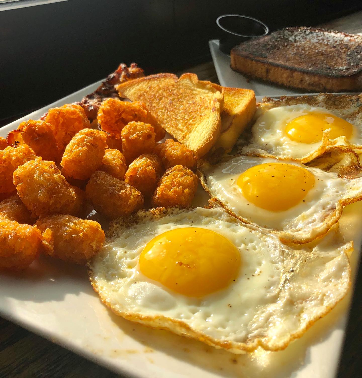 fried eggs, tater tots, toast, bacon, and french toast on a plate