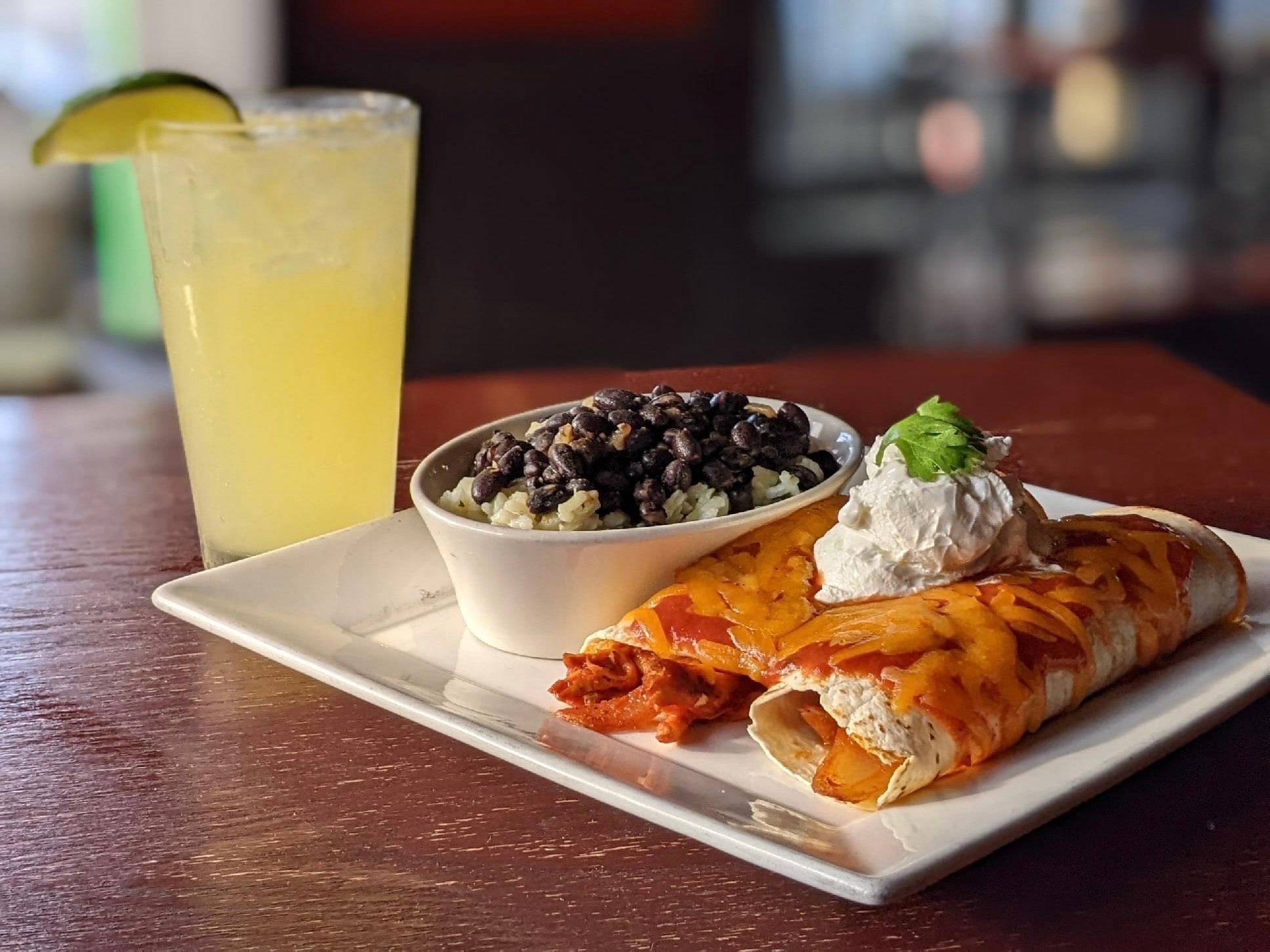 Enchiladas and black beans with rice along side mixed drink