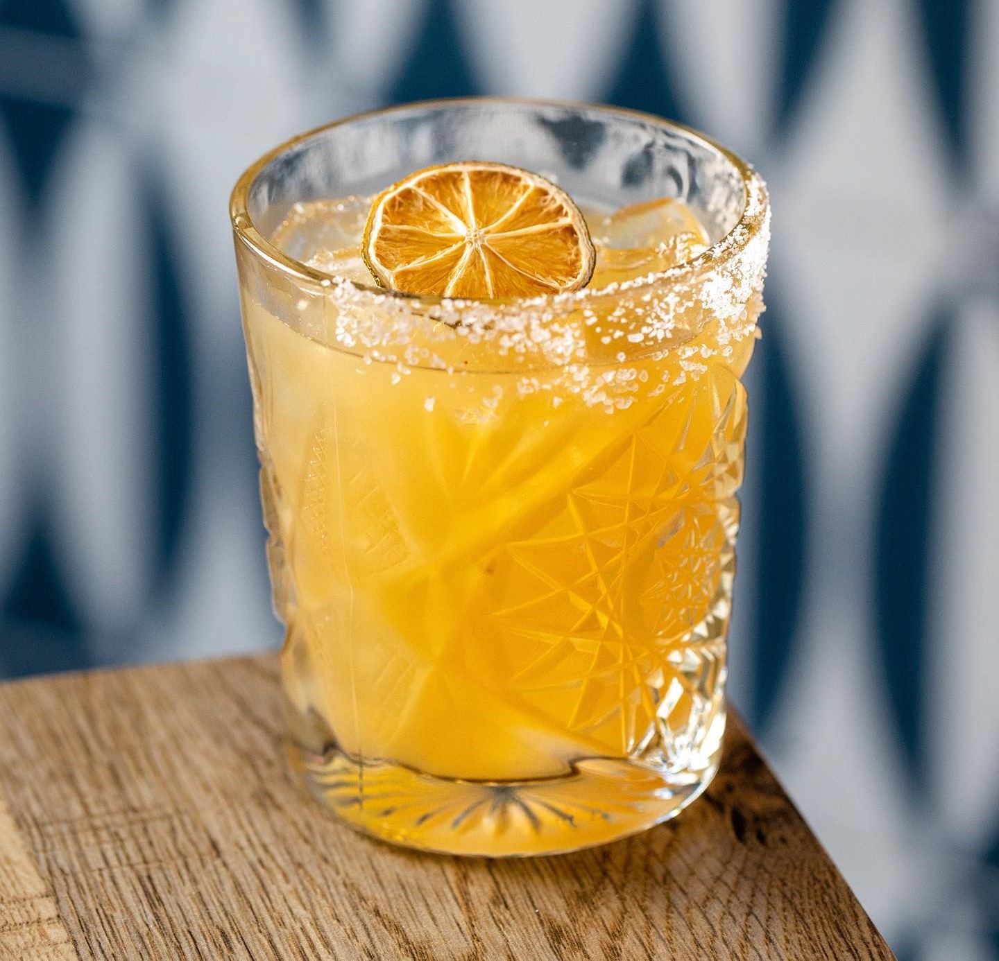 an orange cocktail with a half salted rim and a dried orange wheel