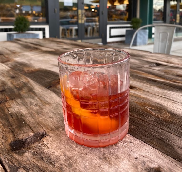 a red drink with a citrus peel on a table