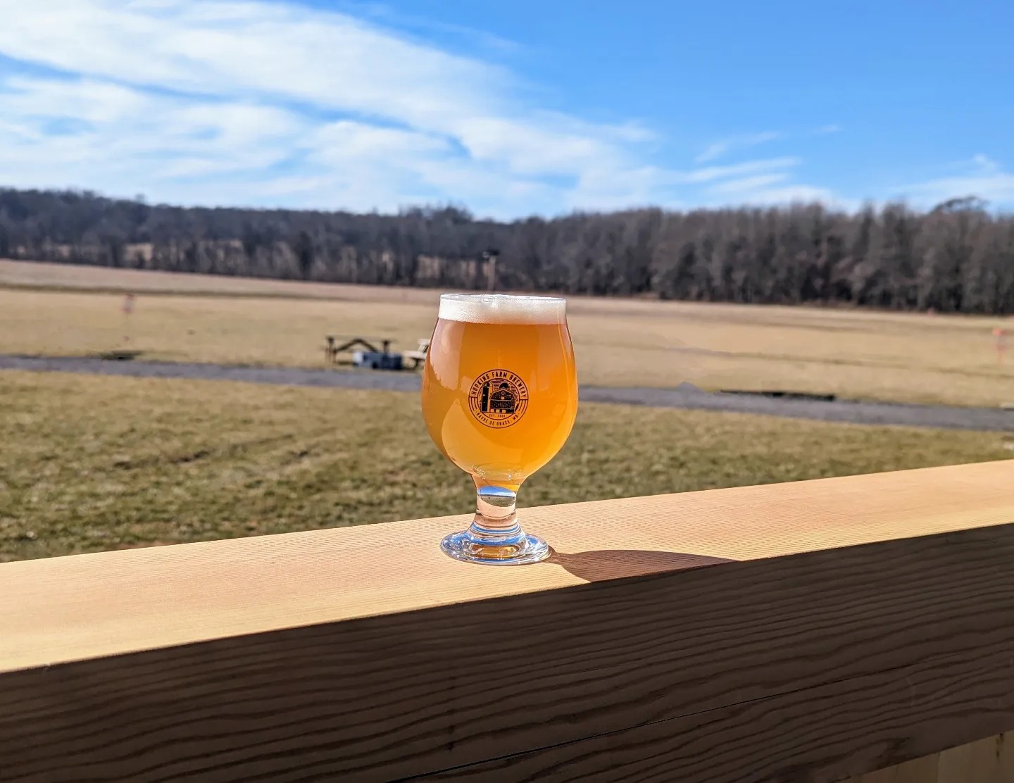 a glass of beer on a porch railing looking over the farm