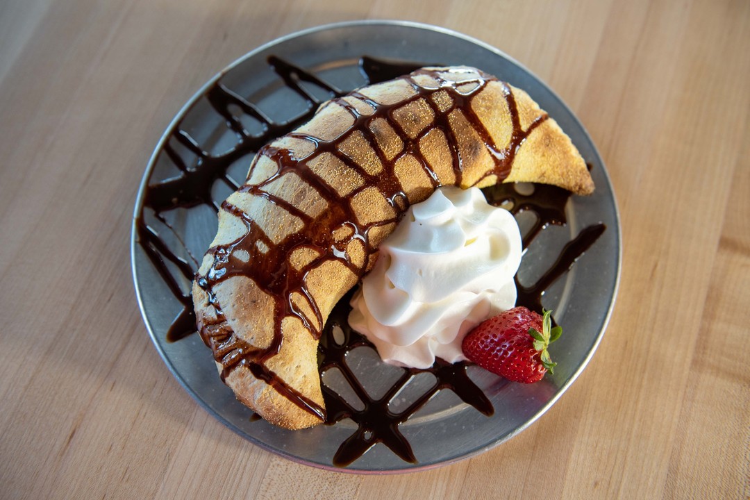 a dessert nutella calzone with whipped cream, chocolate drizzle, and a strawberry