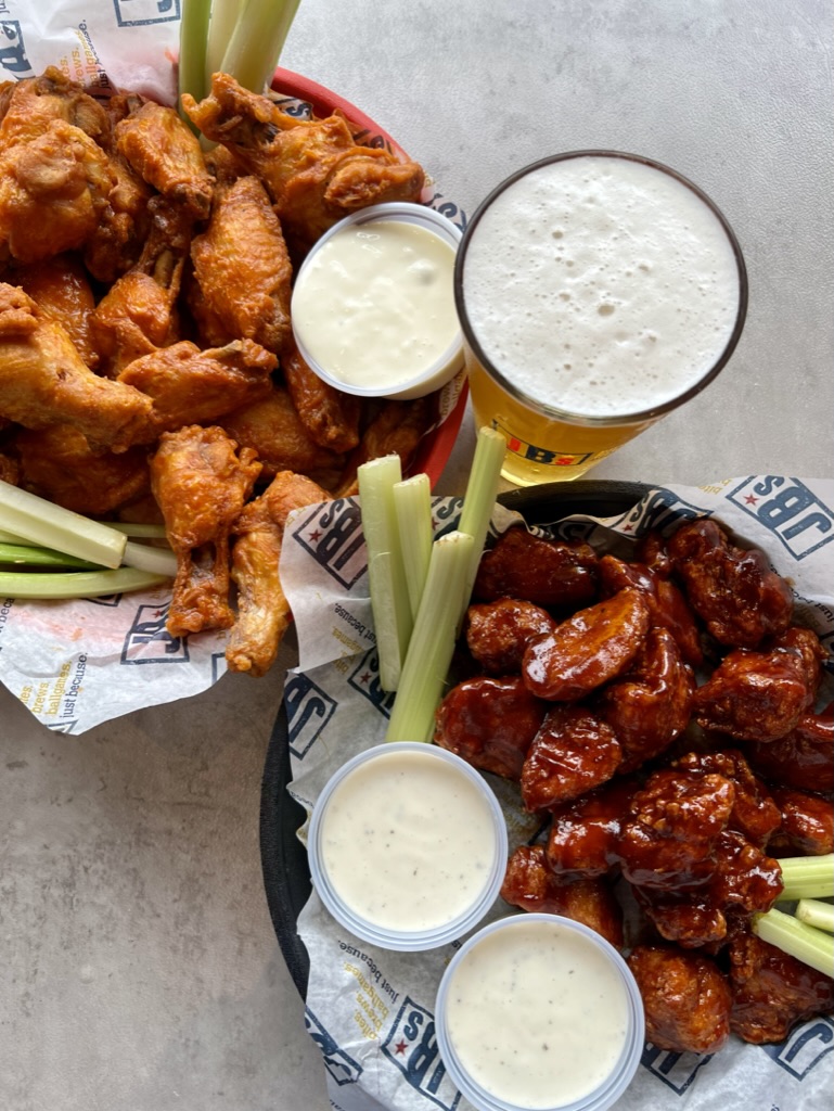 two plates of wings with celery and dips and a glass of beer