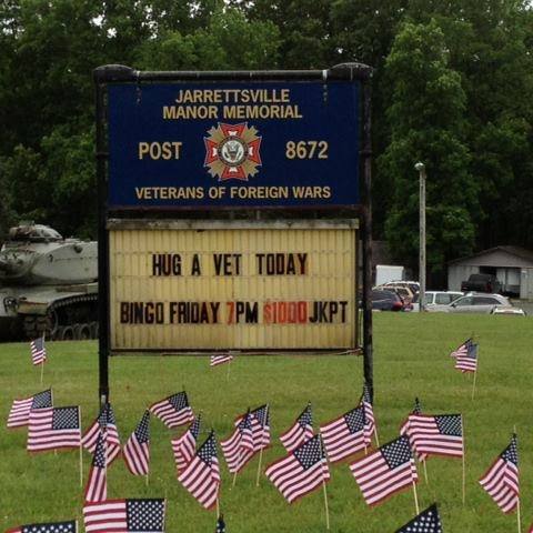 a sign outside the VFW with US flags in the lawn surrounding it
