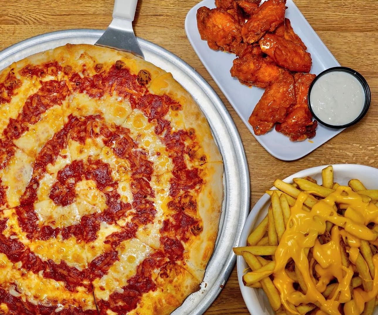 a cheese pizza, a plate of wings with dip, and a bowl of cheesy fries