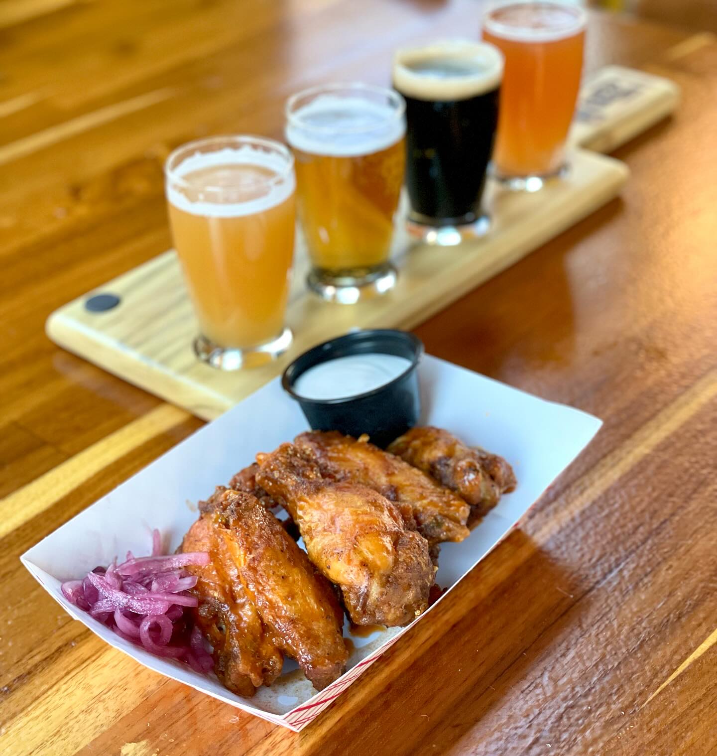 a plate of wings with red onions and dip, and a flight of beer