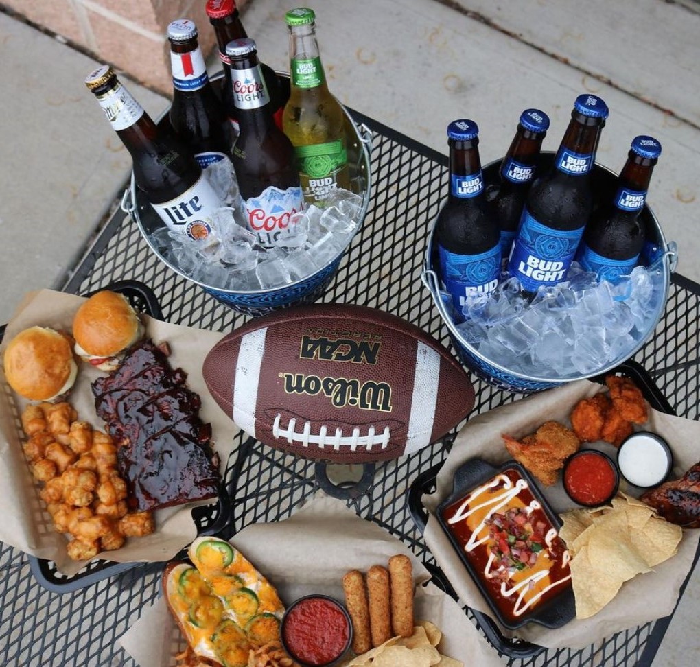 two beer buckets, three trays of food, and a football on a table
