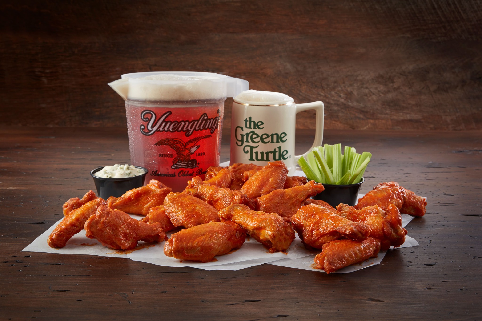 a pitcher and a mug of beer and a pile of wings with celery and dip