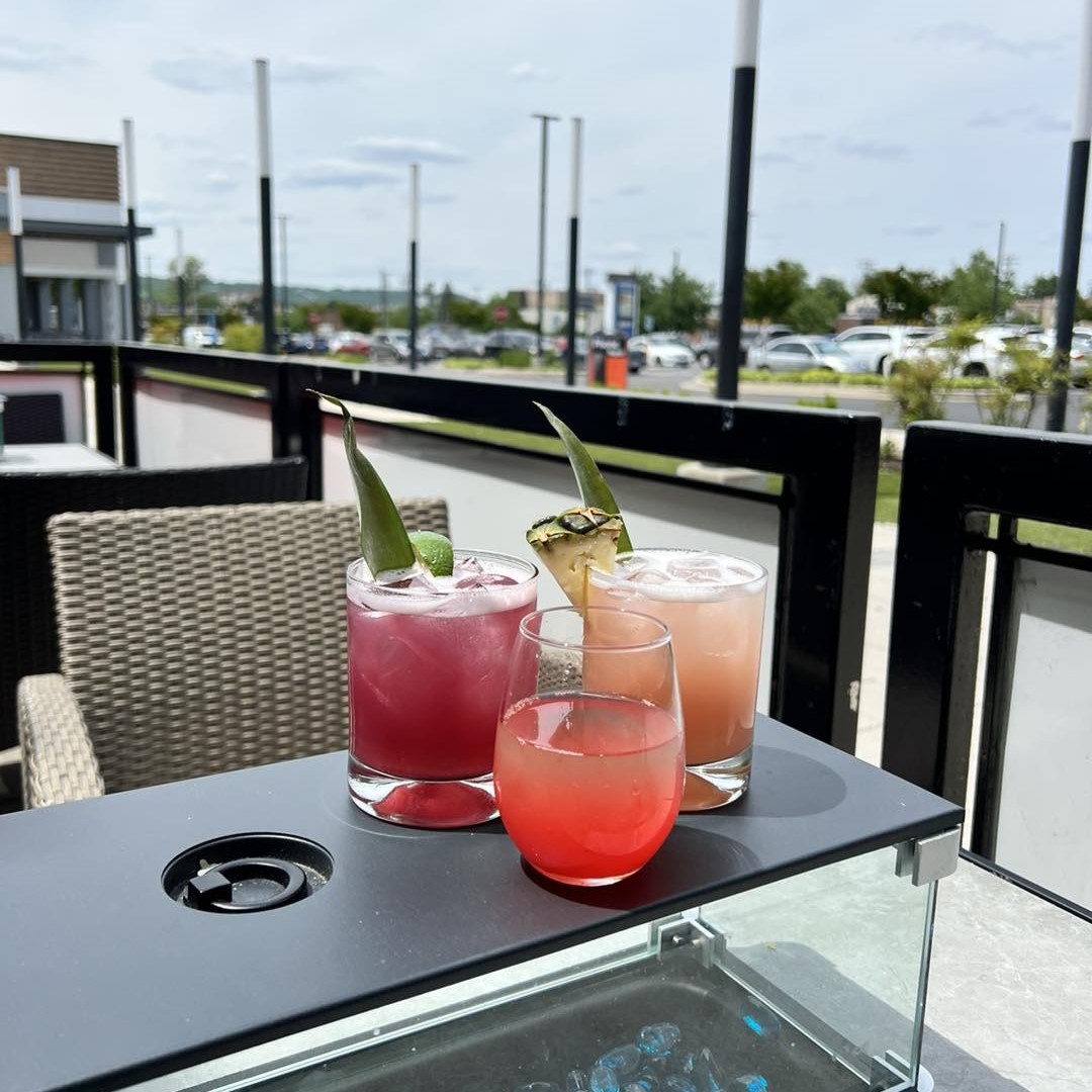 a blueberry margarita with a lime wedge, a bravo bomb, and a kiwi guava margarita with a pineapple wedge on a table outside