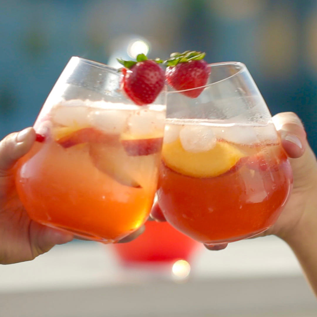 two people cheersing their peach and strawberry cocktails