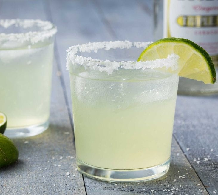 two margaritas with lime wedges and a salted rim