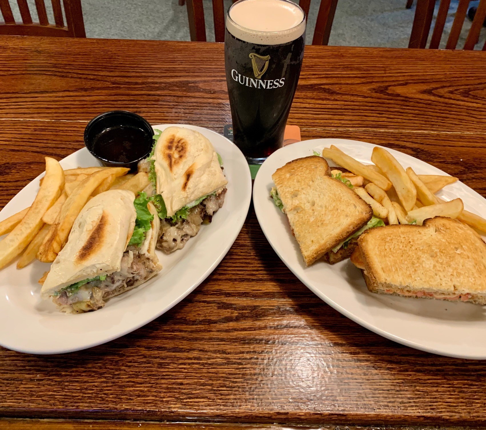 a ribeye cheesesteak sandwich with fries, a next door salmon BLT with fries, and a glass of Guinness