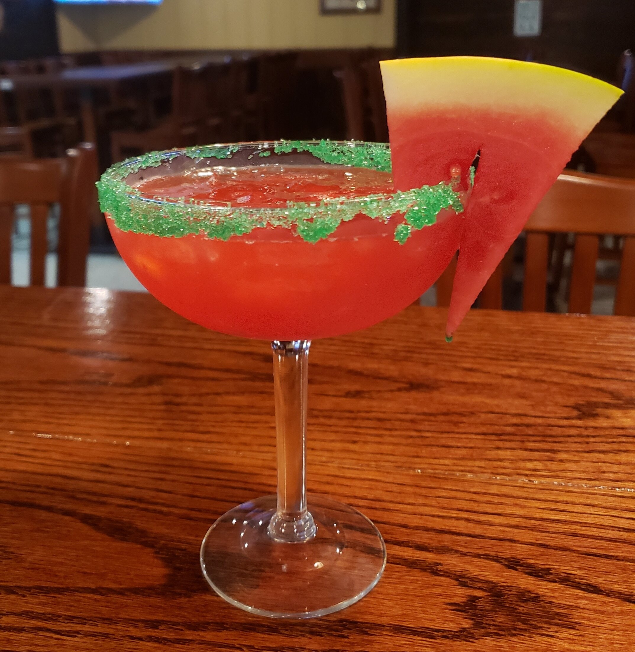 a red drink with a slice of watermelon and a green sugar rim