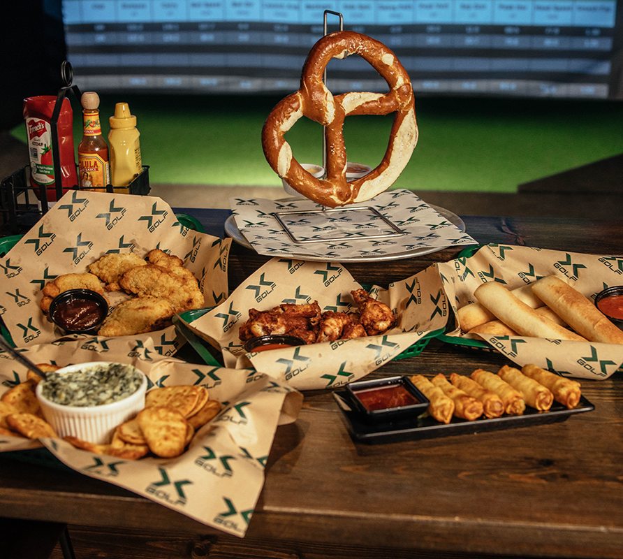 several plates of food on a table, including a soft pretzel, artichoke dip, and wings